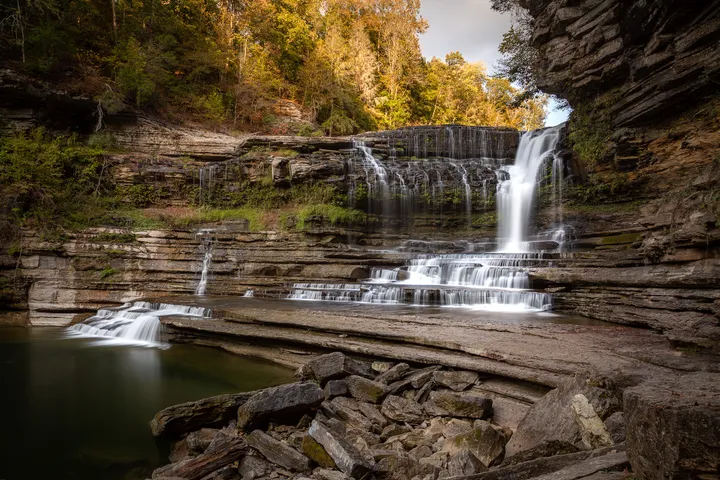 Tiered waterfall cascading over layered rock shelves in autumn light